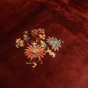 Deep red, high-pile rug featuring central pink and blue floral motifs and white fringe on wood flooring.