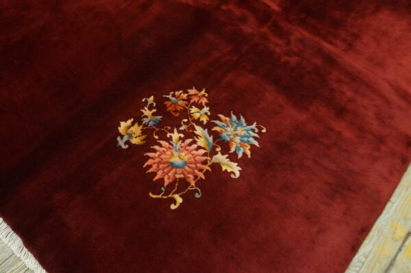 Deep red, high-pile rug featuring central pink and blue floral motifs and white fringe on wood flooring.