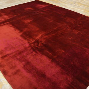 Large, shimmering deep red rug featuring colorful floral motifs in the corners on distressed wood planks.