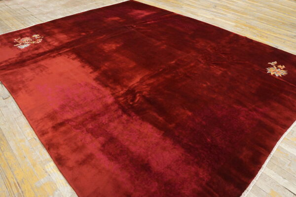 Large, shimmering deep red rug featuring colorful floral motifs in the corners on distressed wood planks.