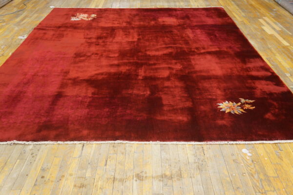 High-sheen burgundy rug with minimal floral corner motifs lies on distressed yellow wood planks.