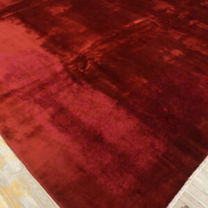 Deep red rug featuring high sheen, visible shading, and small colorful floral corner designs on wood flooring.