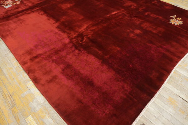 Deep red rug featuring high sheen, visible shading, and small colorful floral corner designs on wood flooring.