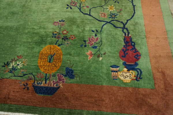Green rug with colorful flowers, vases, and an orange medallion, framed by a wide brown border.