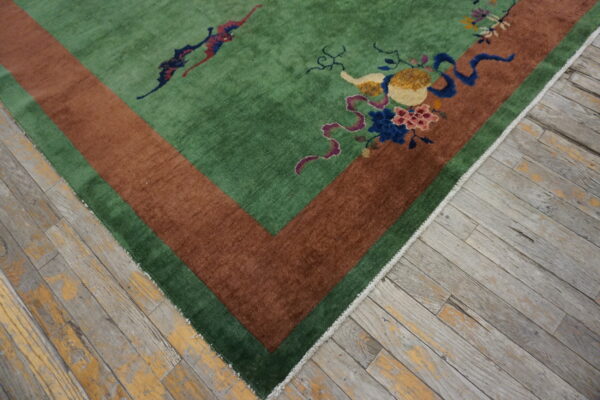 Plush green rug featuring a wide rust border and multicolored floral motifs sits on distressed wood planks.