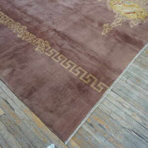 Mauve high-pile rug with tan meander and cloud borders rests on gray distressed wood flooring.