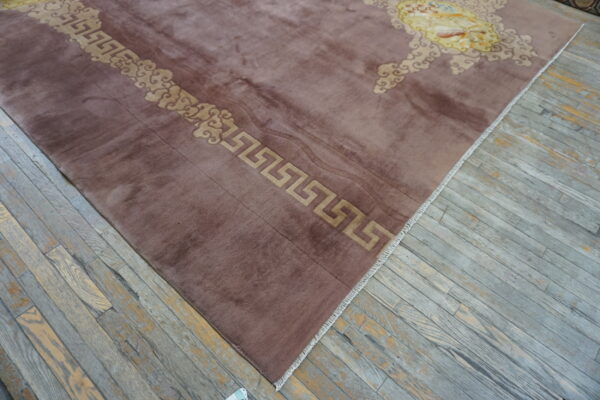 Mauve high-pile rug with tan meander and cloud borders rests on gray distressed wood flooring.