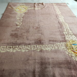 Low-pile dusty pink rug with embossed cream cloud motifs and complex colorful corner medallions on tile.