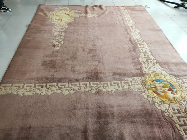 Low-pile dusty pink rug with embossed cream cloud motifs and complex colorful corner medallions on tile.