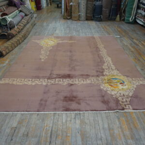Shimmery mauve rug with elaborate beige and yellow abstract patterns displayed on a worn wood floor.