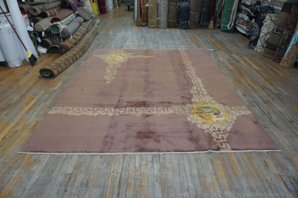 Shimmery mauve rug with elaborate beige and yellow abstract patterns displayed on a worn wood floor.