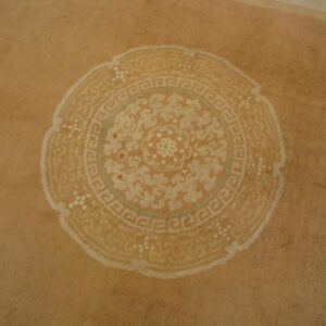 Tan rug featuring a faded round medallion with cream floral and Greek key patterns, accented by teal.