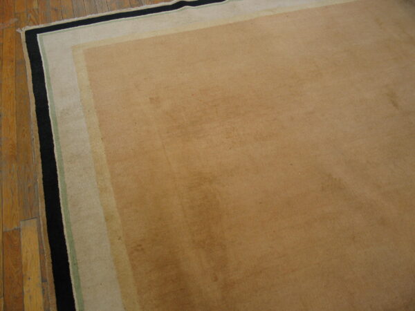 A low-pile tan rug featuring stepped borders of tan, green, and black, sitting on hardwood flooring.
