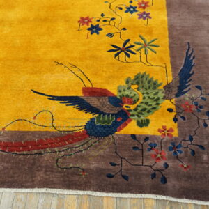 High-pile yellow rug displaying a colorful bird and floral design bordered in brown on wood flooring.