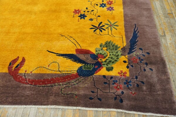 High-pile yellow rug displaying a colorful bird and floral design bordered in brown on wood flooring.
