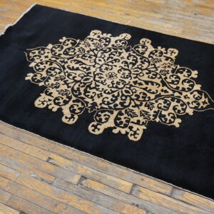 Black area rug with a contrasting tan ornate design centered on worn hardwood floors.