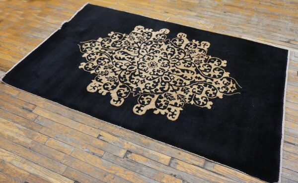 Black area rug with a contrasting tan ornate design centered on worn hardwood floors.
