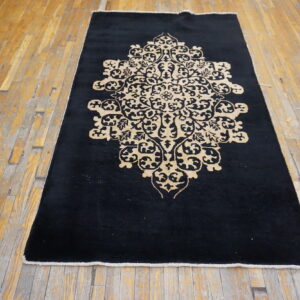 Black rug featuring a large beige medallion is placed on worn wooden plank flooring.