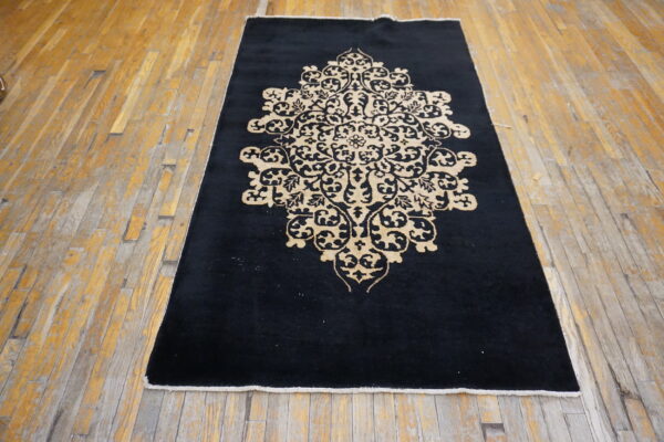 Black rug featuring a large beige medallion is placed on worn wooden plank flooring.
