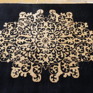 Black rug with a central beige scrolling floral medallion laid on a light-colored floor.