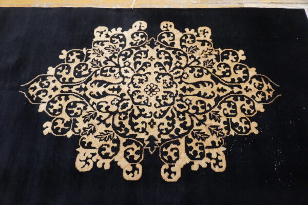 Black rug with a central beige scrolling floral medallion laid on a light-colored floor.