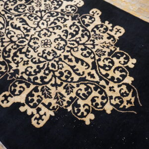 A high-contrast black rug with a large tan medallion featuring detailed floral scrollwork rests on rustic wood planks.