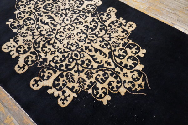 A high-contrast black rug with a large tan medallion featuring detailed floral scrollwork rests on rustic wood planks.