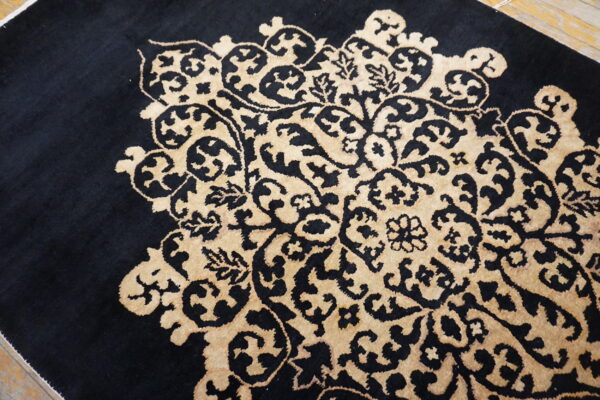 Close-up of a rug featuring a black, medium-pile background with a raised tan floral medallion pattern.