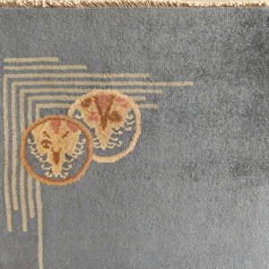 Dusty blue rug corner shows beige geometric lines and overlapping tan and pink circular flower designs.