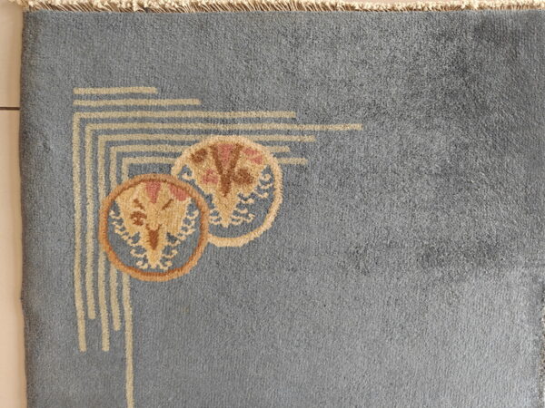 Dusty blue rug corner shows beige geometric lines and overlapping tan and pink circular flower designs.