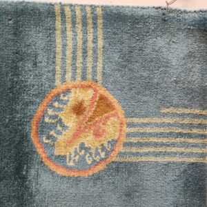 Textured blue rug featuring beige stripes, an orange and gold circular medallion, and natural fringe.