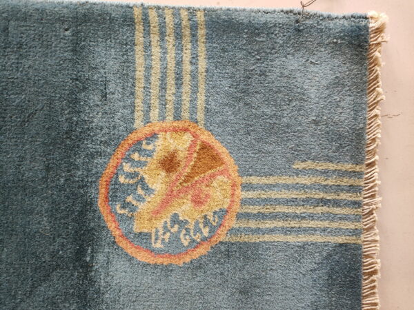 Textured blue rug featuring beige stripes, an orange and gold circular medallion, and natural fringe.