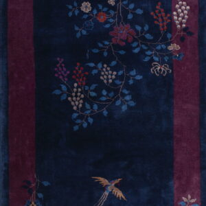 Navy blue rug with a magenta border patterned with vibrant flowers, vines, and a central gold bird motif.