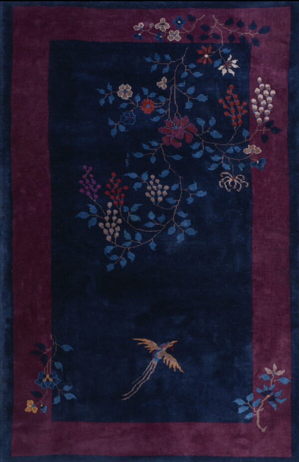 Navy blue rug with a magenta border patterned with vibrant flowers, vines, and a central gold bird motif.