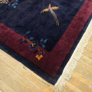 Navy blue rug with stylized gold bird and blue flowers bordered by maroon on a light wood floor.