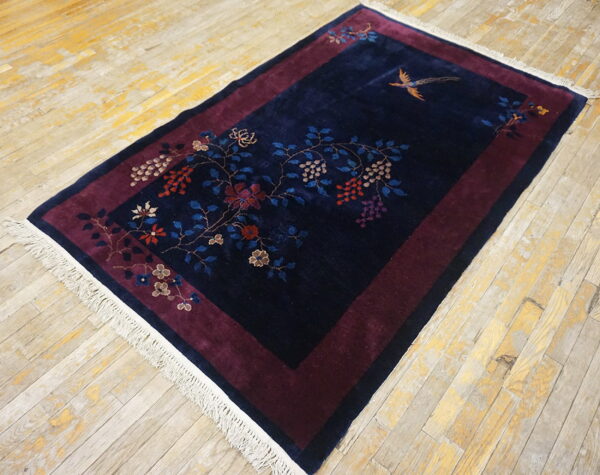 Navy blue rug with a burgundy border features floral and bird motifs on distressed wood planks.