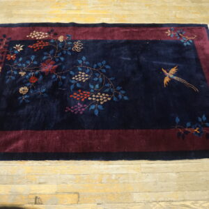 Plush navy rug featuring maroon borders and vibrant botanical patterns with a golden bird on light wood planks.
