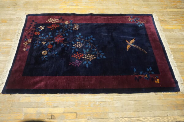 Plush navy rug featuring maroon borders and vibrant botanical patterns with a golden bird on light wood planks.