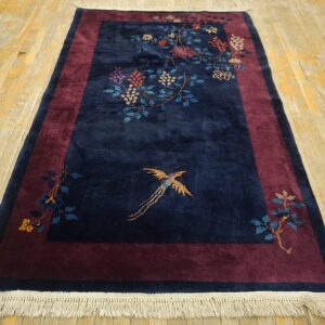 Velvety navy rug with floral vines and gold bird sits on distressed light wood plank flooring.