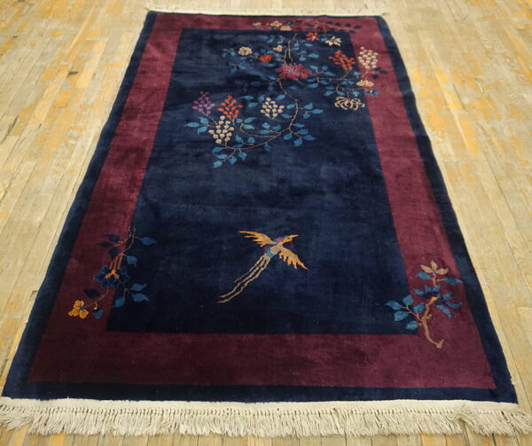 Velvety navy rug with floral vines and gold bird sits on distressed light wood plank flooring.