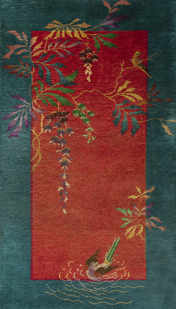 Teal and red rug with a sculpted pile and a botanical pattern of colorful vines, leaves, and a bird.