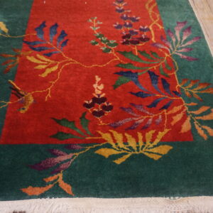 A runner rug featuring a red field and green border with intricate multicolored florals lies on rustic wood flooring.