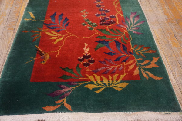 A runner rug featuring a red field and green border with intricate multicolored florals lies on rustic wood flooring.