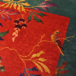 Red and green rug featuring a colorful floral motif with vines, leaves, and a small yellow bird.