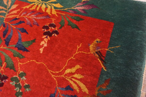 Red and green rug featuring a colorful floral motif with vines, leaves, and a small yellow bird.