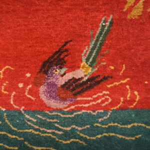 Detail of a medium-pile rug featuring a purple and black waterfowl motif on a red field with green and yellow waves.