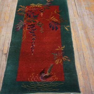 Red and green runner rug featuring a detailed pattern of vines, flowers, and a swimming bird on worn wooden planks.