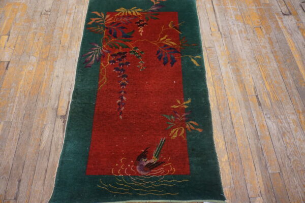 Red and green runner rug featuring a detailed pattern of vines, flowers, and a swimming bird on worn wooden planks.