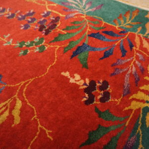 The red and green rug with multi-colored floral patterns rests on light wood flooring.