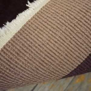 Rolled rug detail shows dark brown, cream fringe, and ribbed tan stripes on distressed wood floor.